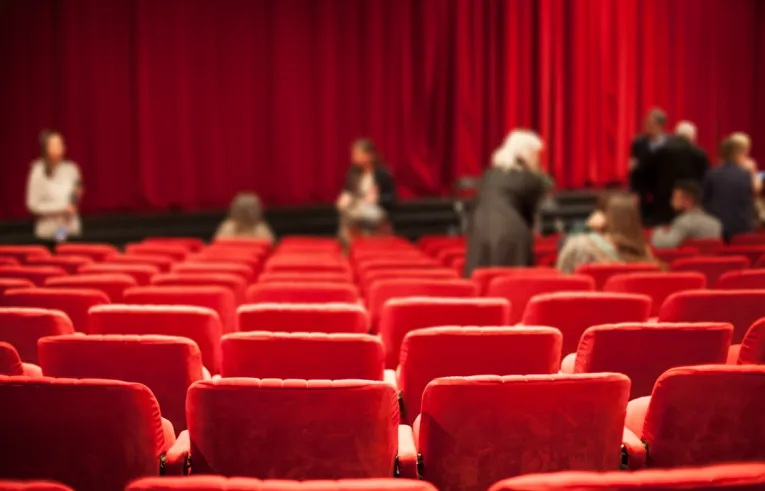 Sala teatralna z czerwonymi fotelami i czerwoną kurtyną. 