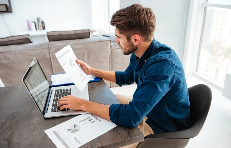 Mężczyzna przy biurku pracuje na laptopie i przegląda dokumenty