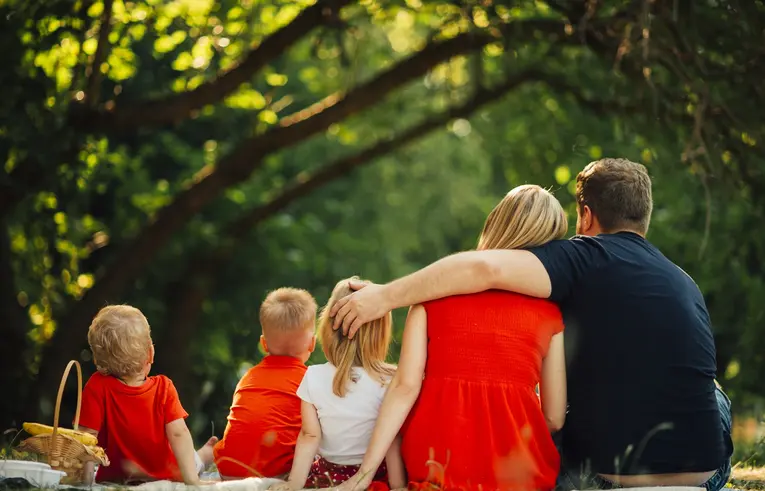 Pięcioosobowa rodzina na pikniku w lesie, na kocu siedzą rodzice i troje dzieci