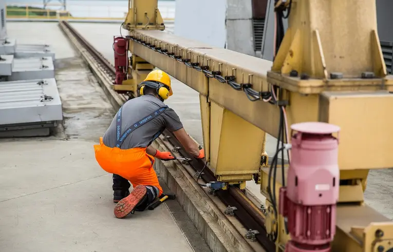 Mężczyzna w stroju roboczym w kasku i nausznikach dokręca kluczem śruby w maszynie 