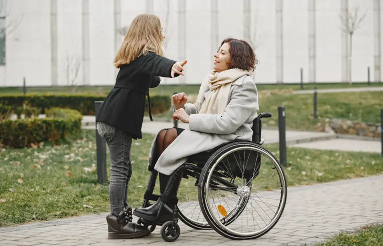 Stojąca kobieta wskazuje coś ręką przed kobietą siedzącą na wózku inwalidzkim
